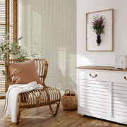 Rattan chair with a pink pillow and white blanket in a room with a white cabinet and framed picture on the wall.