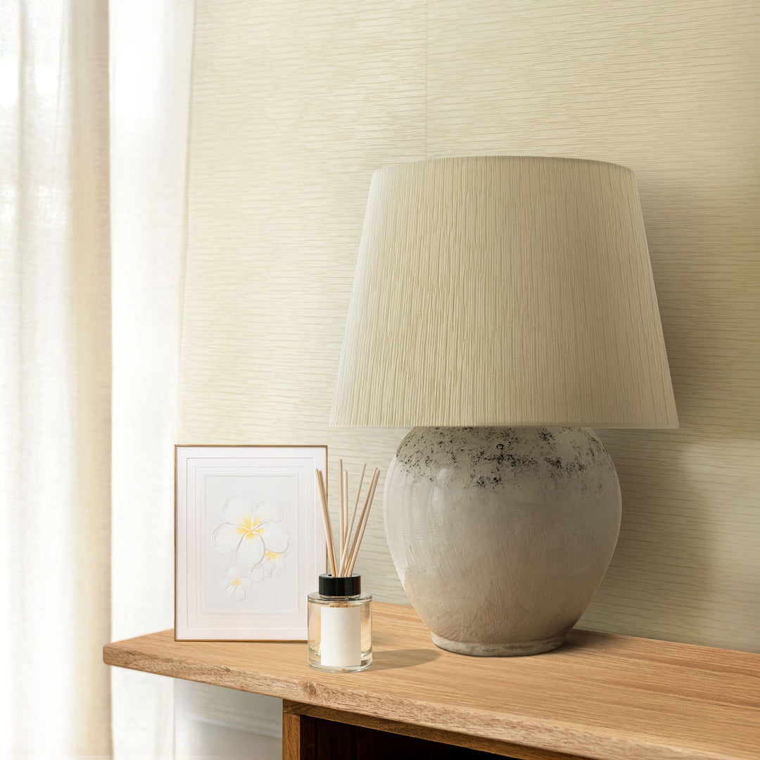 Decorative lamp on a wooden table with a framed picture and diffuser bottle against a neutral wall.