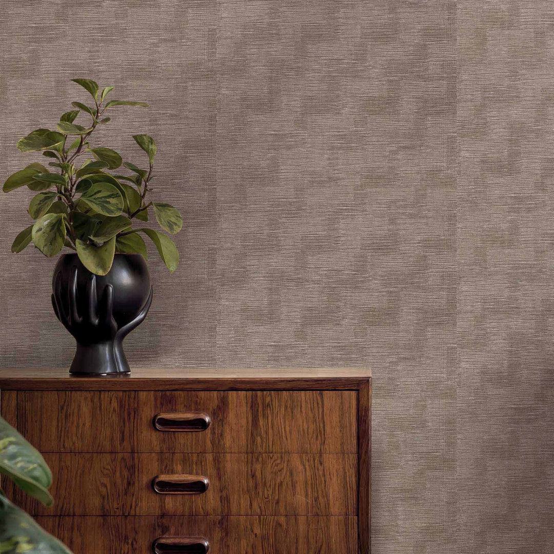 Wooden dresser with a black vase and plant against a textured brown wall