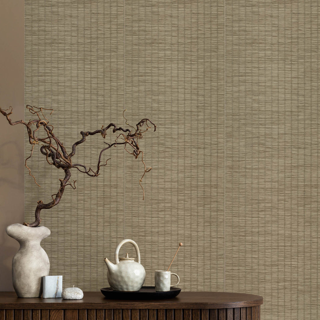 Decorative setting with a teapot, cup, and branch against a textured wall.