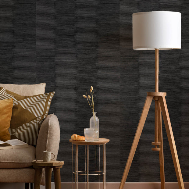 Modern living room with a tripod lamp, sofa, and side table against a dark textured wall.