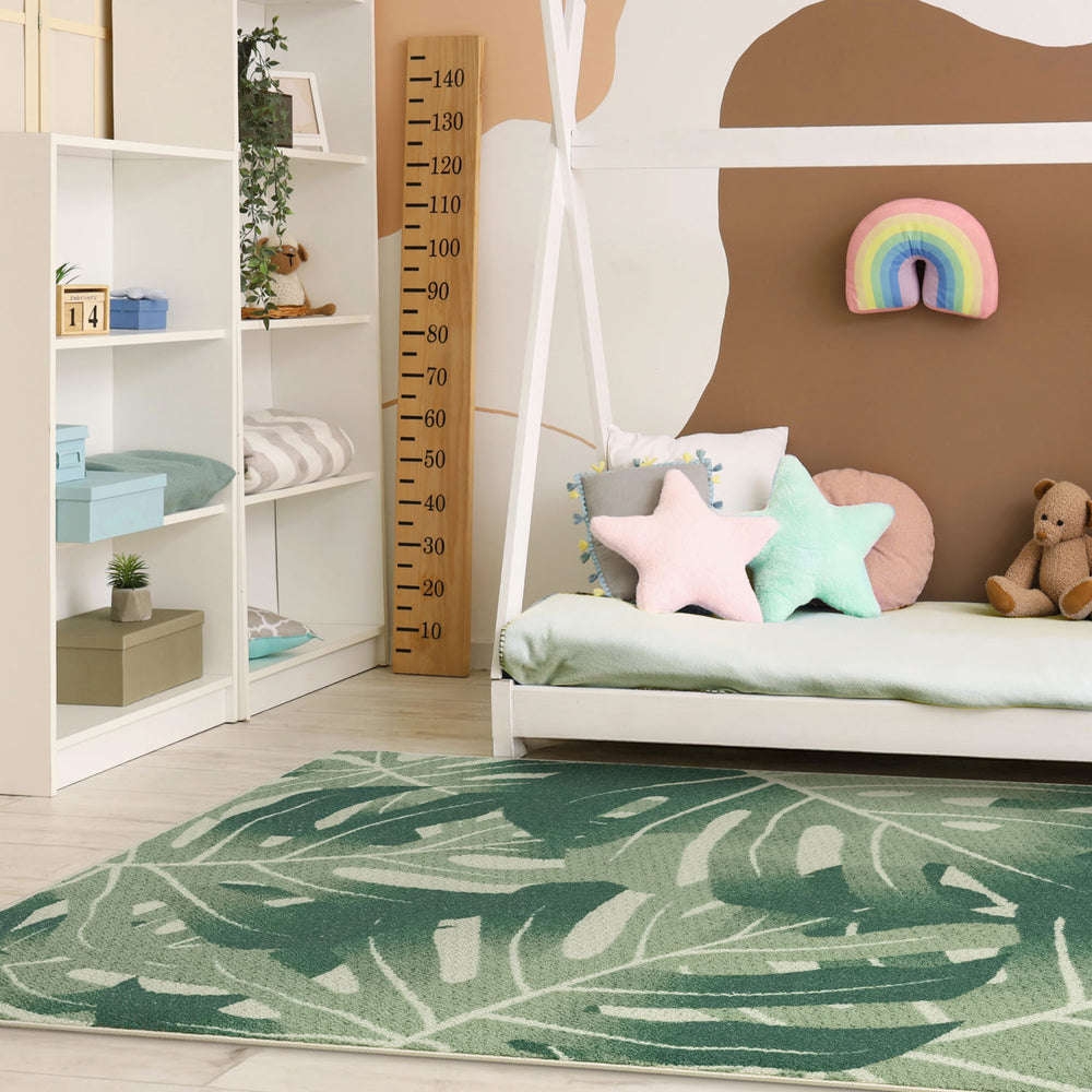 Children's room with a bed, pillows, and a green leaf-patterned rug.