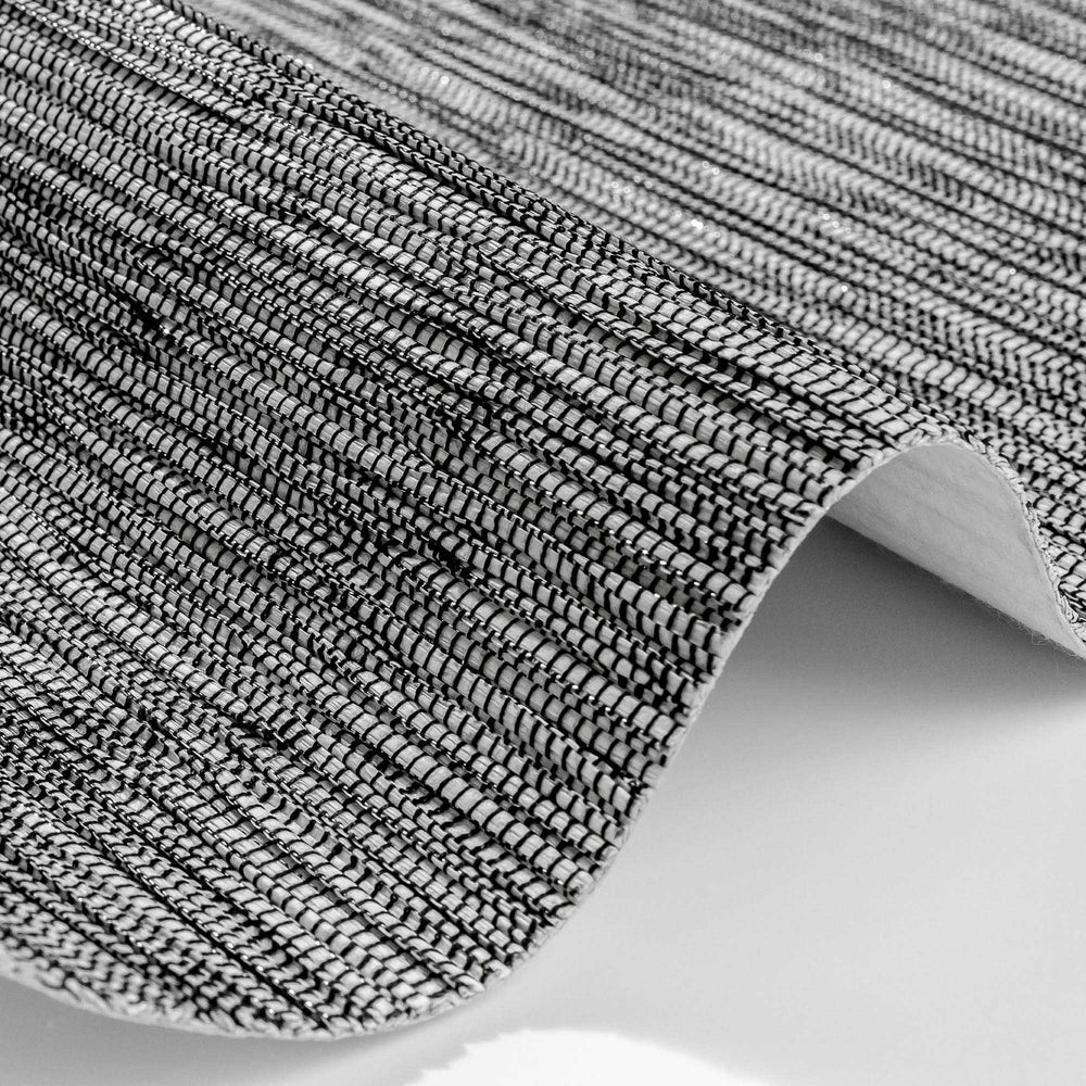 Close-up of a textured wallpaper with a black and silver woven pattern, showcasing intricate horizontal and vertical threads that create a shimmering, fabric-like surface. The wallpaper is slightly curved to display its flexibility and material detail.