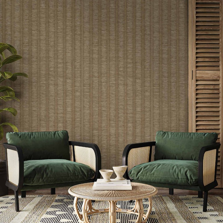 Neutral brown striped textured wallpaper in a modern living room with green velvet armchairs, rattan accents, and a round woven coffee table.