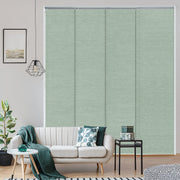 Living room with a white sofa, green cushions, and a plant, featuring a large window with green blinds.