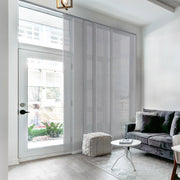Modern living room with gray sofa, white ottoman, and large window with blinds.