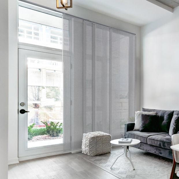 Modern living room with gray sofa, white ottoman, and large window with blinds.