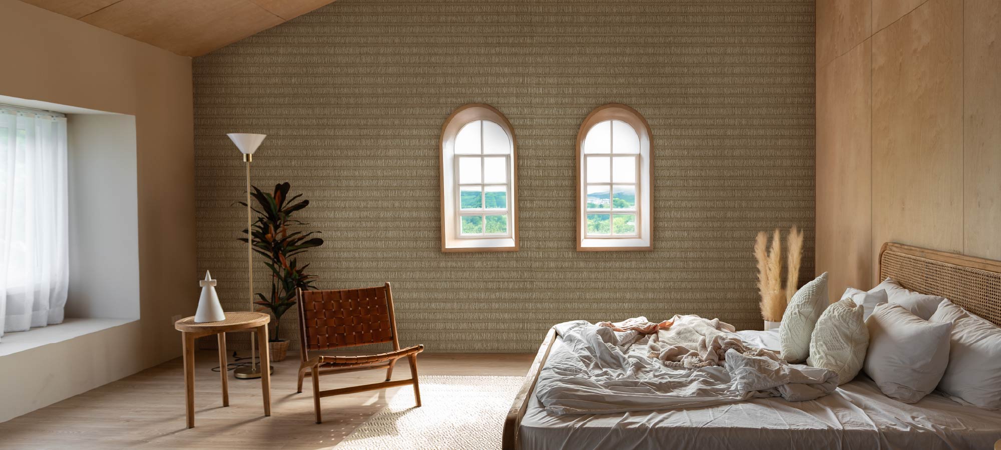 Cozy modern bedroom with arched windows, woven accent chair, neutral textured wallpaper, and unmade bed with soft pillows in natural sunlight.