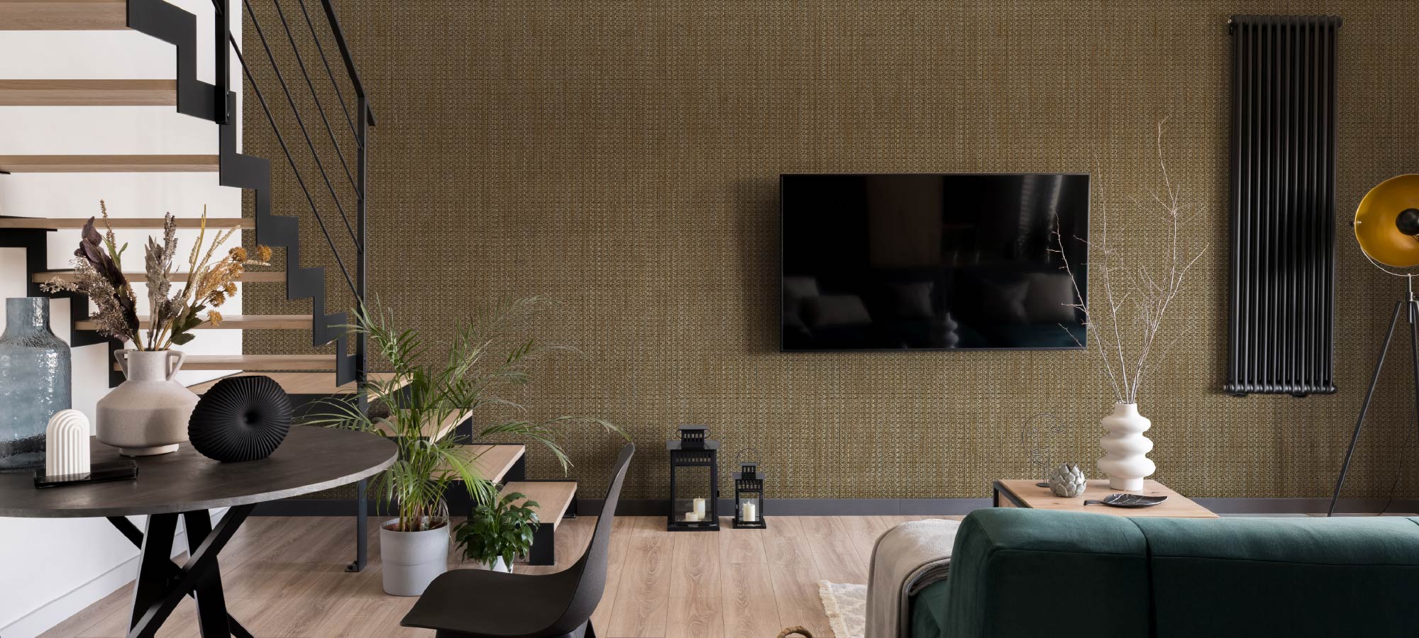 Stylish living room with woven textured wall, flat screen tv, modern staircase with black railing, indoor plants, and minimalist decor accents.