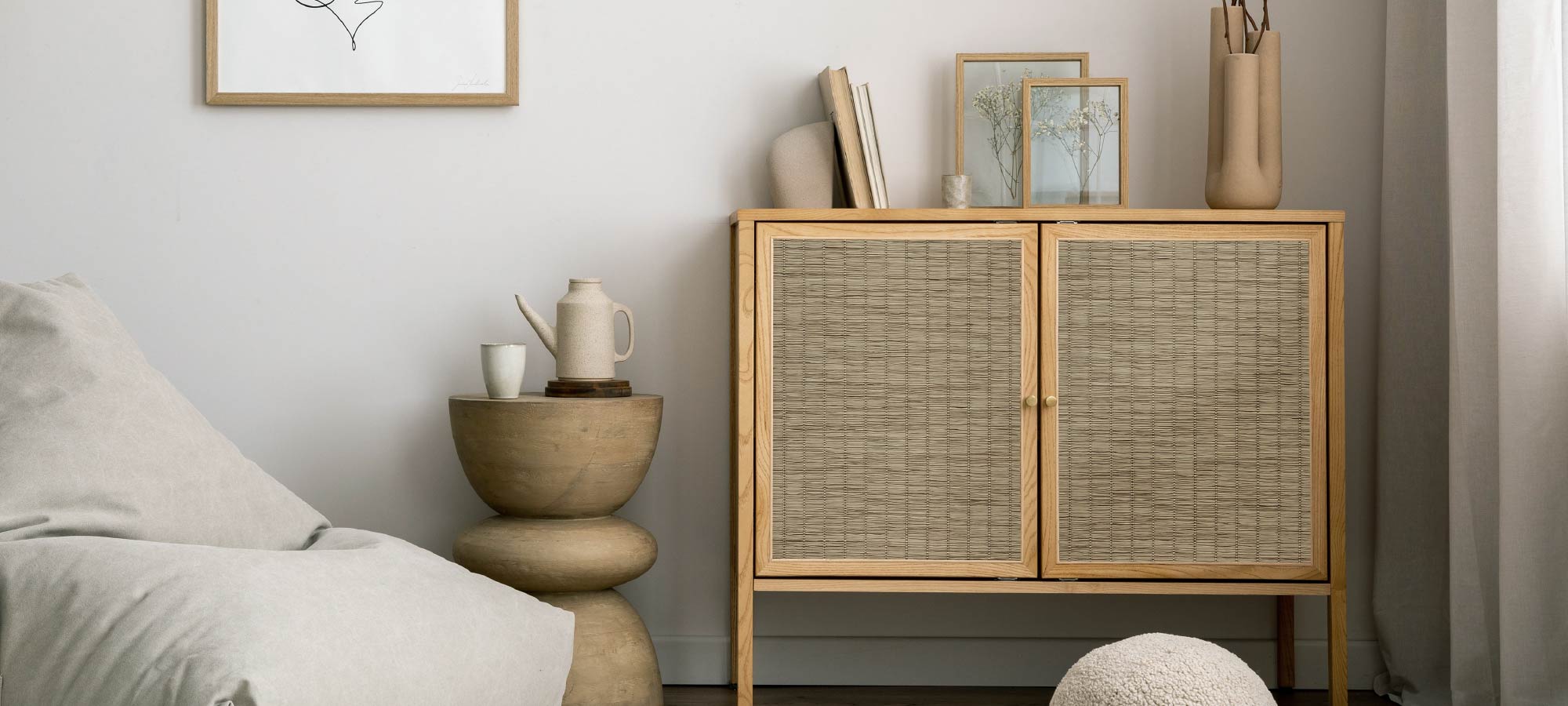 Cozy minimalist living room with natural wood storage cabinet, soft neutral armchair, and decorative ceramic vase.