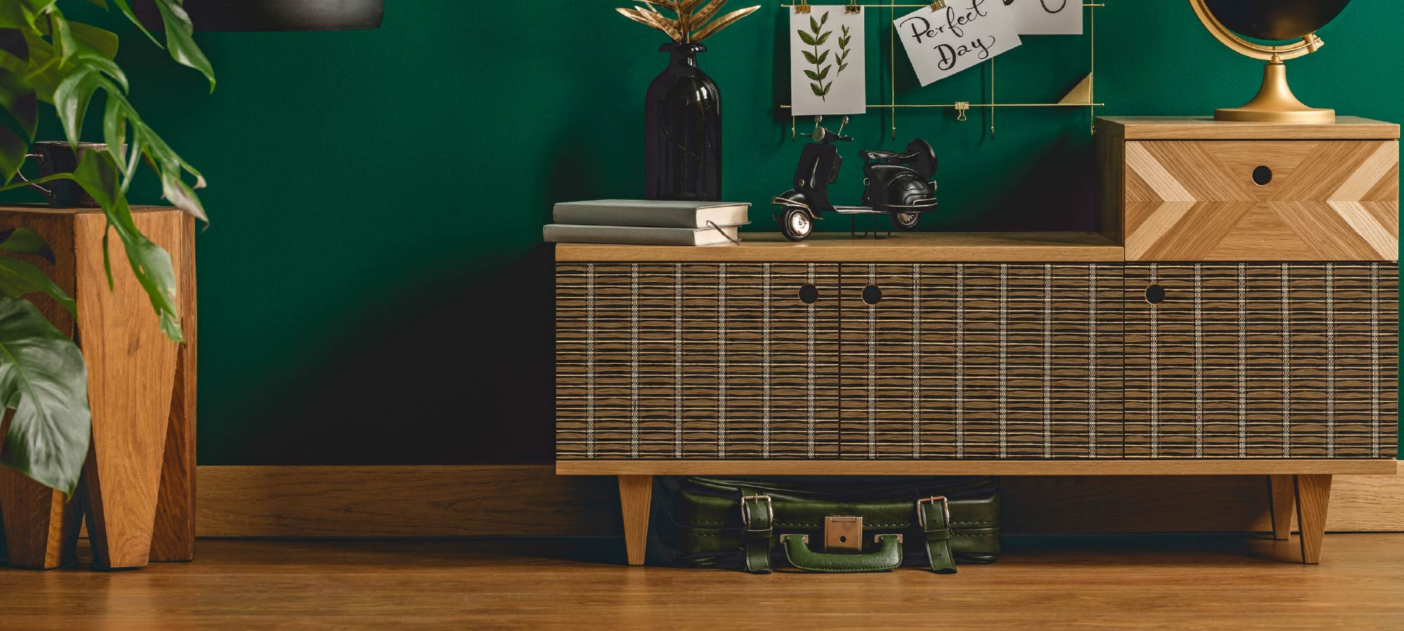 Stylish mid-century storage cabinet with woven doors, dark green accent wall, decorative globe, and indoor plants.