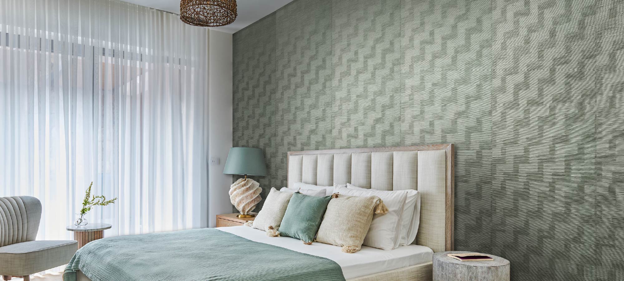 Modern bedroom interior with upholstered headboard, textured green accent wall, soft pillows, and natural light from sheer curtains.