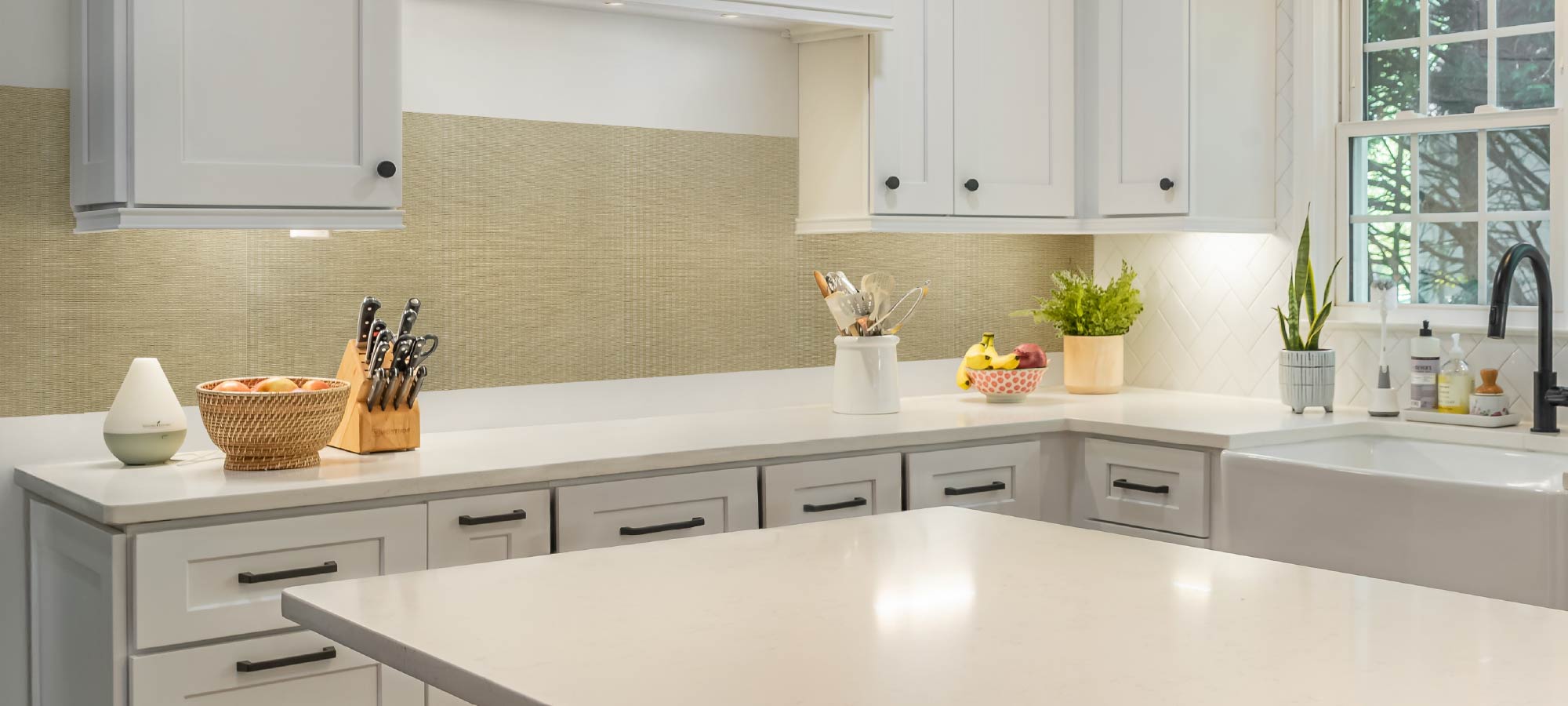 Modern kitchen with white cabinets, a tiled backsplash, and various kitchen items on the counter.