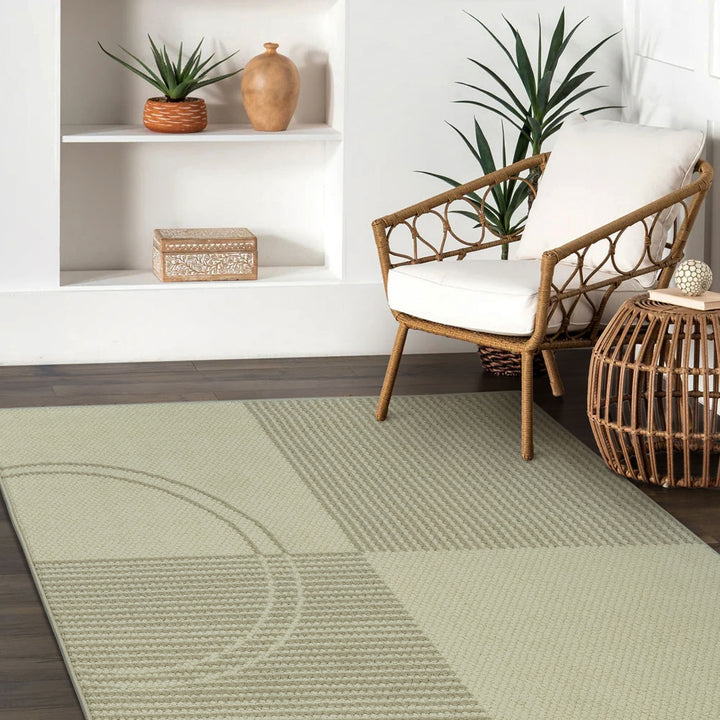 Green rug with geometric pattern in a room with a chair and shelves.