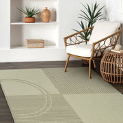 Green rug with geometric pattern in a room with a chair and shelves.