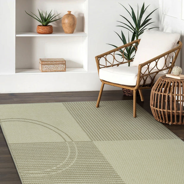 Green rug with geometric pattern in a room with a chair and shelves.