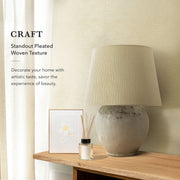 A modern, well-lit living space with a light beige, textured wall covering from GoDear Design. The image emphasizes the "CRAFT Aesthetic Lifestyle" by pairing the decorative material with a large, rustic ceramic table lamp, a framed floral print, and a wooden table. The text highlights the product's "Standout Pleated Woven Texture" and its ability to add artistic taste and beauty to a home.