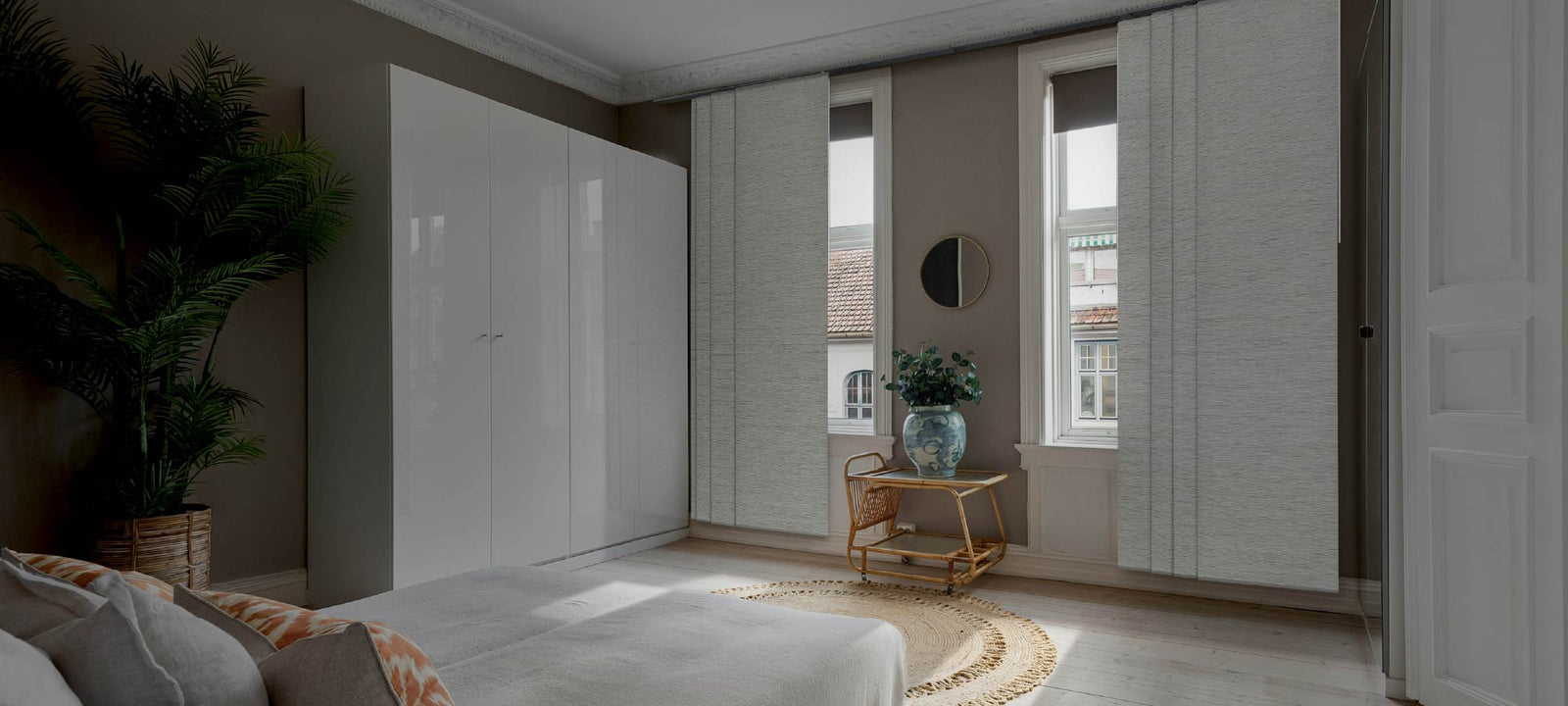 Modern bedroom with white wardrobes, a bed, decorative elements, and blackout window treatments.