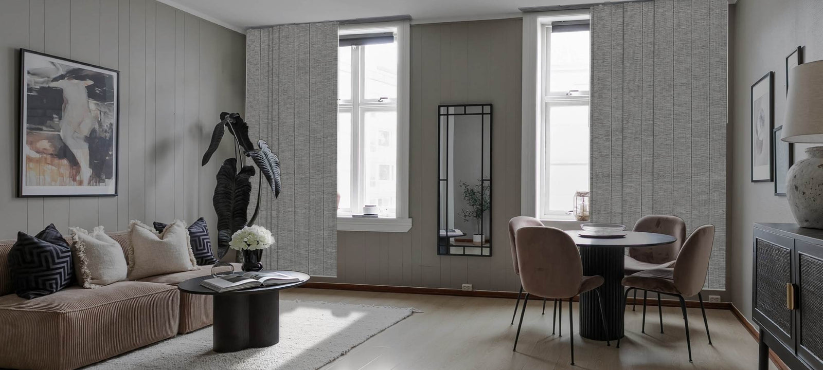 Cozy living and dining corner with vertical textured panels, velvet taupe dining chairs, abstract artwork, and a soft corduroy sofa styled with layered cushions, evoking a calm and contemporary mood.