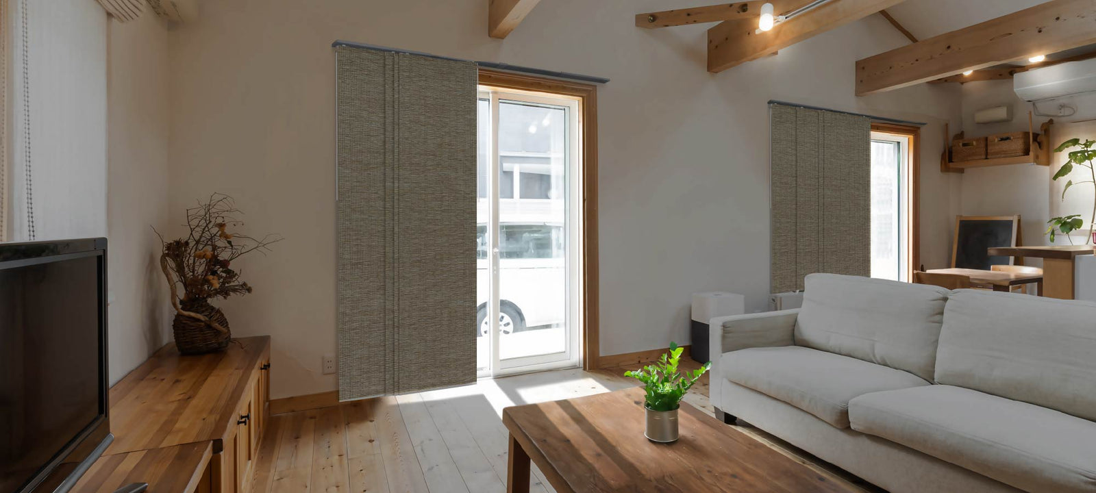 Scandinavian-inspired living room with exposed wood beams, a light cream sofa, and woven privacy panels filtering sunlight through glass doors, creating a tranquil and natural ambiance.