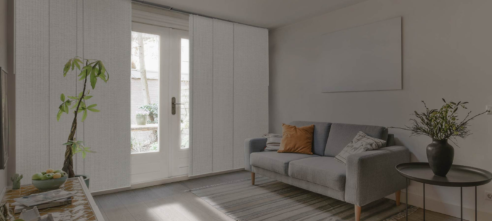 Bright living space featuring a small gray sofa with accent pillows, a natural wood coffee table, and floor-to-ceiling light-filtering panels on French doors, creating a cozy and inviting indoor-outdoor connection.