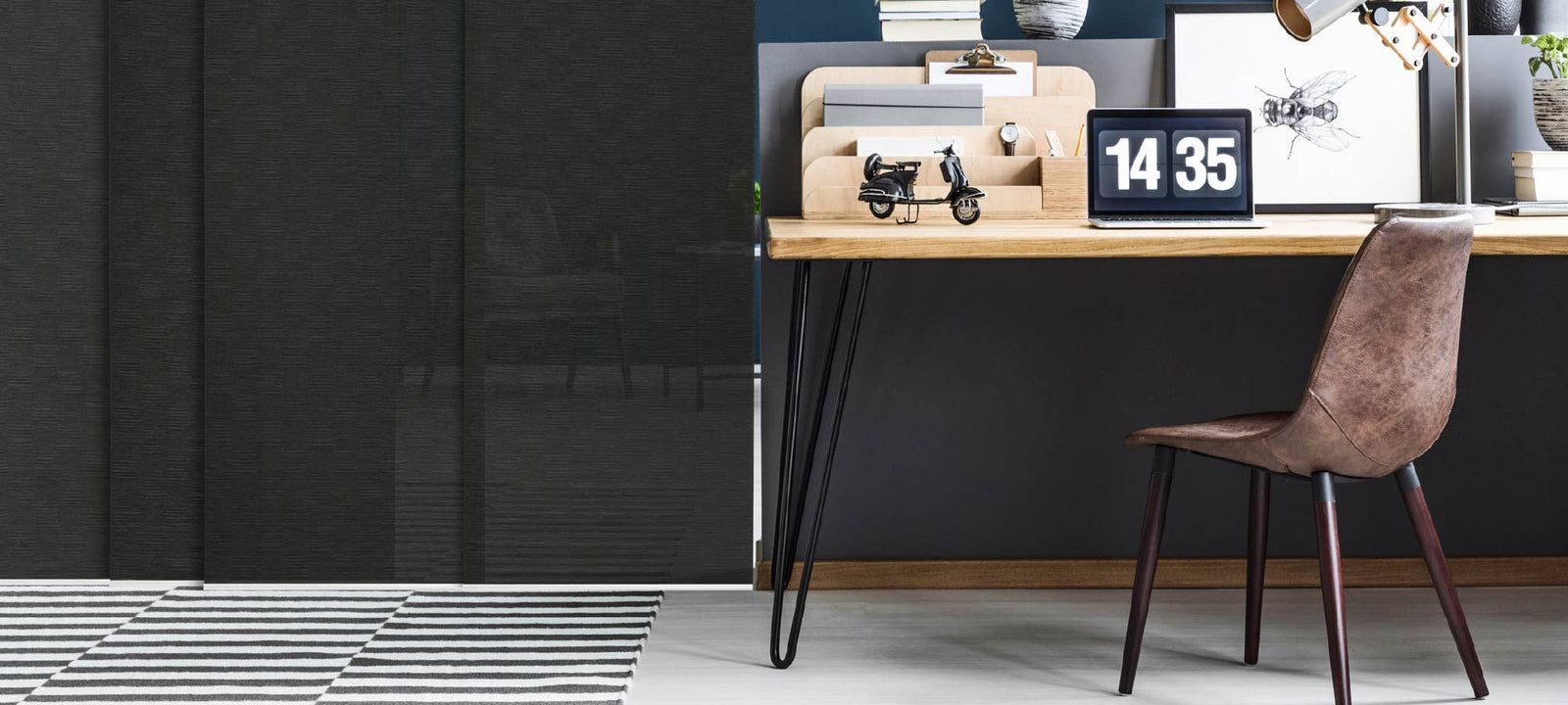 Modern home office with a minimalist wood desk, leather chair, and bold Black King panel blinds that provide sleek privacy and contrast against a striped monochrome rug.