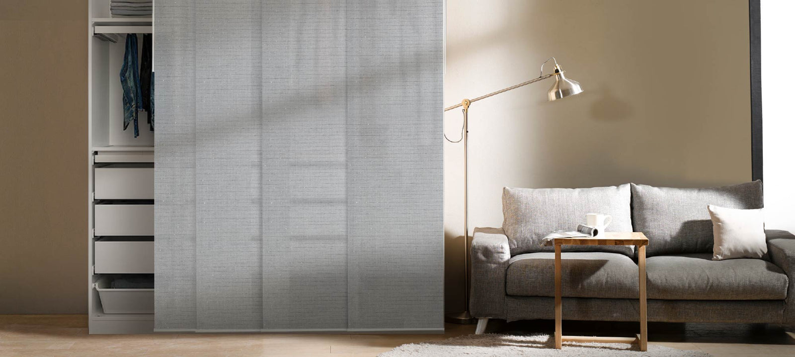 Minimalist interior with Diamond Silver panel blinds covering an open wardrobe. The cool-toned semi-sheer fabric adds subtle shimmer and privacy, paired with a gray couch and clean neutral walls for a calm, modern feel.