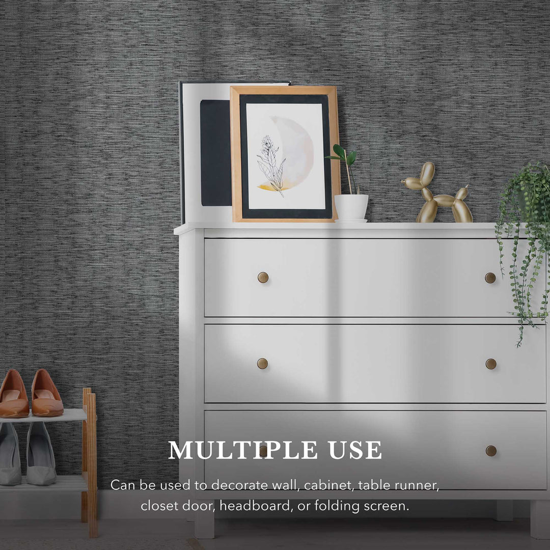White dresser with brass knobs against a dark gray woven textured wallpaper. The dresser top displays framed artwork, a small potted plant, and a gold balloon dog sculpture. A hanging plant drapes from the right side, and a shoe rack with heels is partially visible on the left. Text on the wall reads, “MULTIPLE USE—Can be used to decorate a wall, cabinet, table runner, closet door, headboard, or folding screen.
