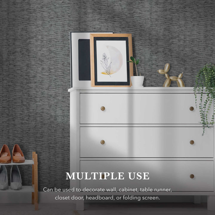 White dresser with brass knobs against a dark gray woven textured wallpaper. The dresser top displays framed artwork, a small potted plant, and a gold balloon dog sculpture. A hanging plant drapes from the right side, and a shoe rack with heels is partially visible on the left. Text on the wall reads, “MULTIPLE USE—Can be used to decorate a wall, cabinet, table runner, closet door, headboard, or folding screen.