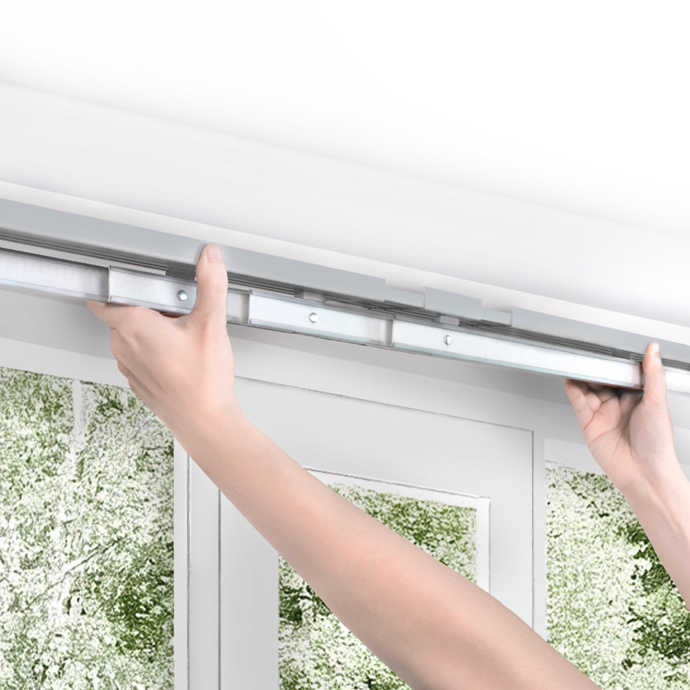 Person adjusting a window blind with a white window and greenery in the background