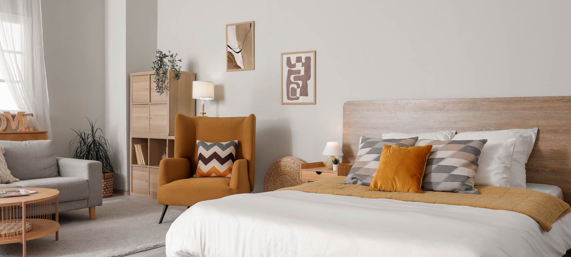 Stylish bedroom interior with wooden headboard, patterned cushions, mustard yellow armchair, and warm neutral tones.