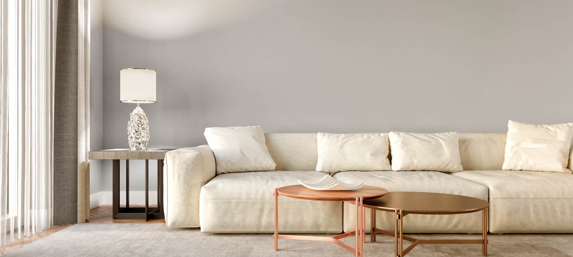 Bright neutral living room with cream sofa, decorative pillows, round metallic coffee tables, and elegant side lamp.