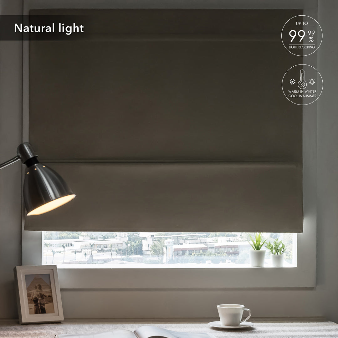 GoDear Design Dark roller blind covering a window with a lamp and cup on a table in the foreground.