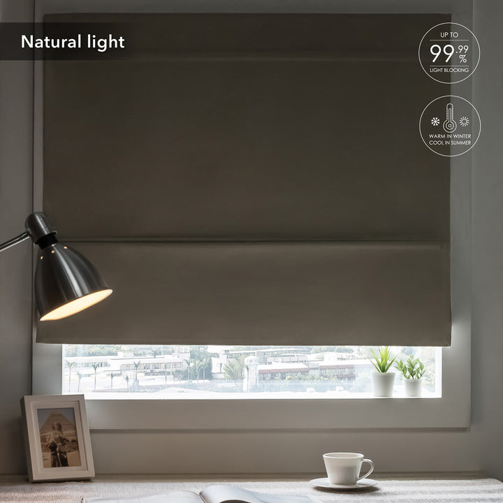 GoDear Design Dark roller blind covering a window with a lamp and cup on a table in the foreground.