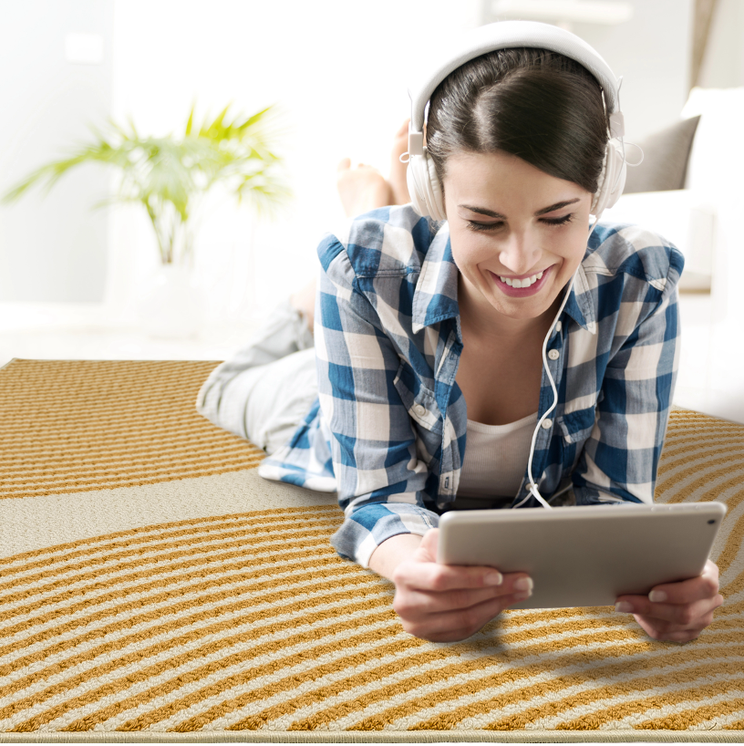 GoDear Design Woman lying on a carpeted floor using a tablet and wearing headphones.