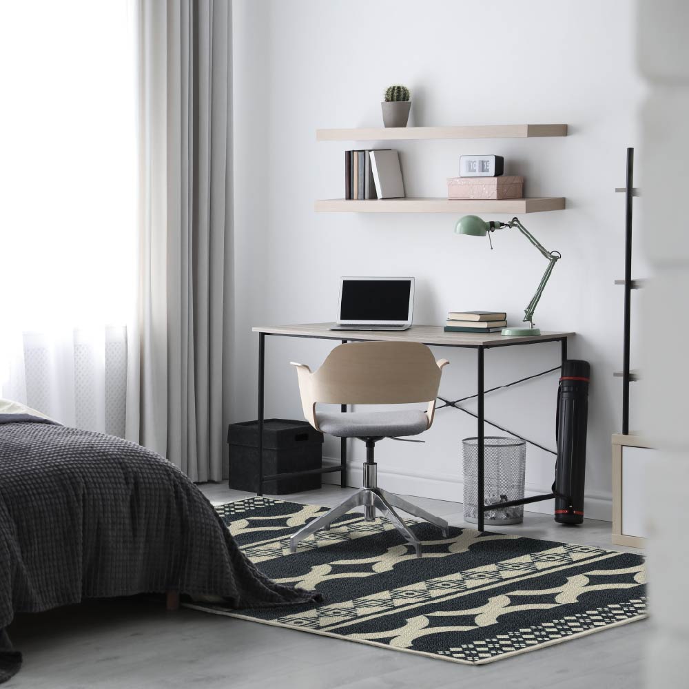 Modern bedroom with a desk, chair, dark wool rug and decorative elements.