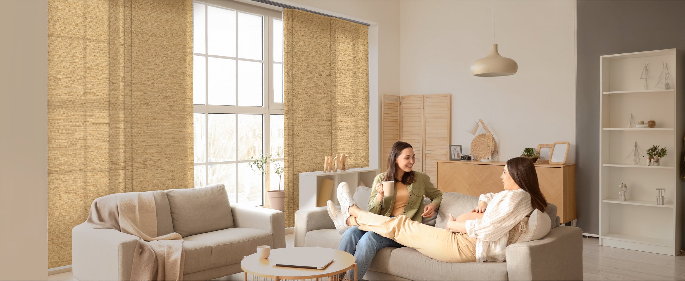 GoDear Design_Two women sitting on a couch in a modern living room with large windows and neutral decor.