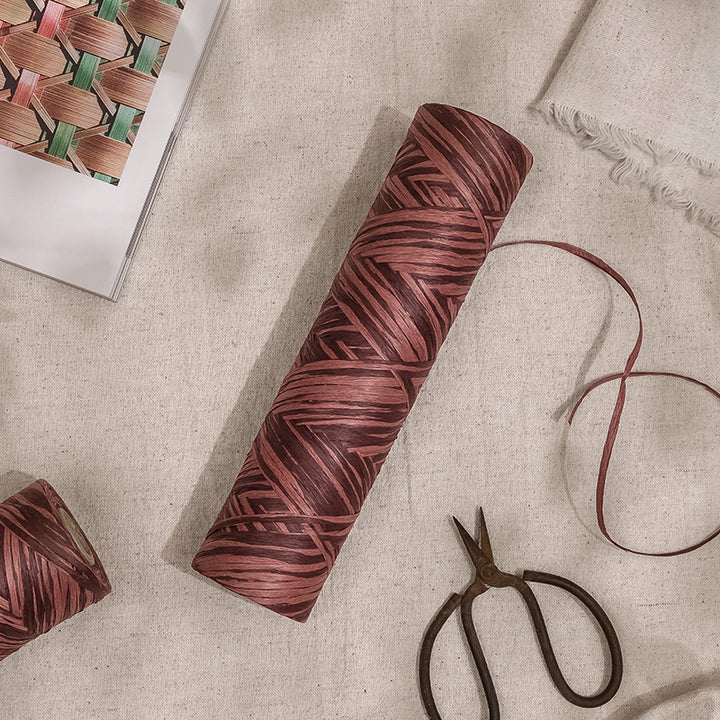 GoDear Design_A roll of carmine-colored paper raffia ribbon with a zigzag pattern, displayed on a beige background alongside scissors and a clip.