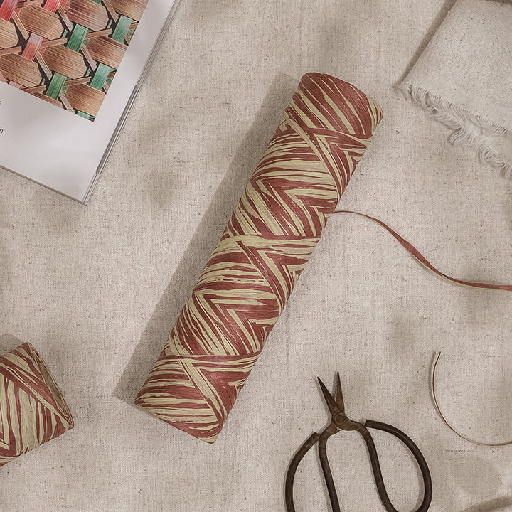 GoDear Design_Rolls of paper raffia ribbon with a zigzag pattern in shades of brown and beige, displayed on a white surface, alongside cutting scissors and a pair of tweezers.