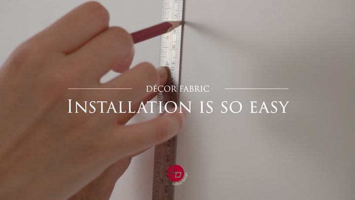 Person applying unpasted wallpaper to a wall using a brush and smoothing tool; wallpaper paste is being applied to the back of the paper before installation.